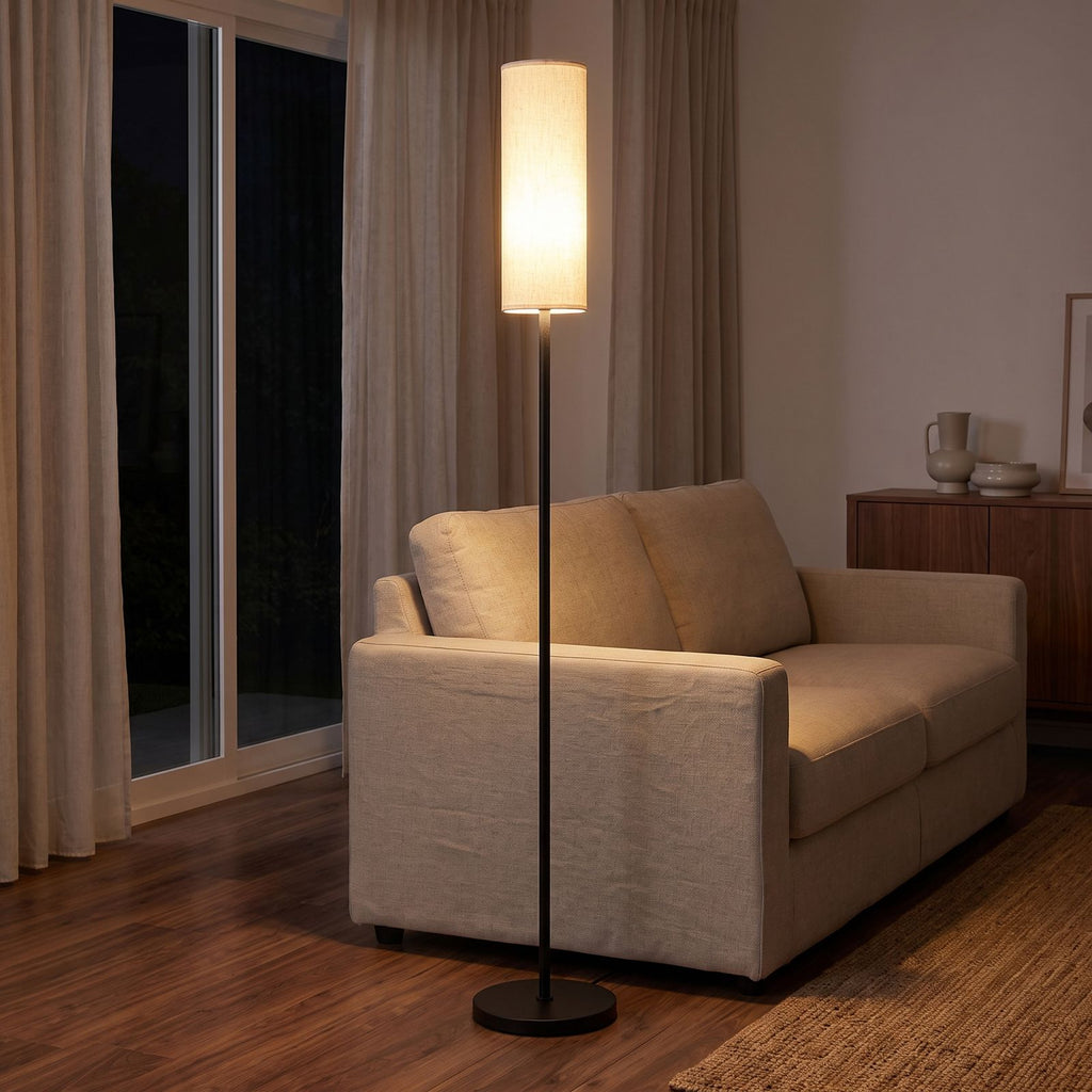 Fabric cylinder shade floor lamp behind a sofa at night