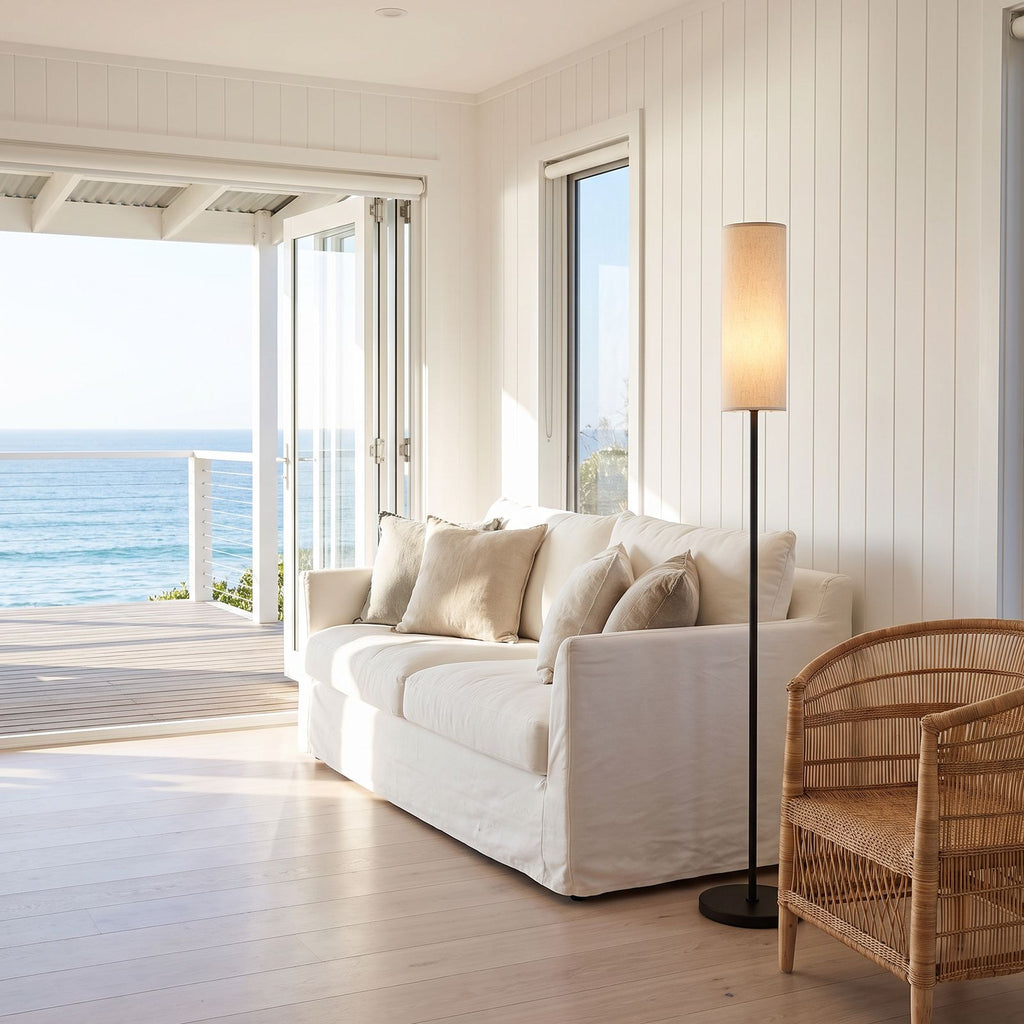 Slim black floor lamp with cream linen shade at the end of a sofa in a coastal beach house living room