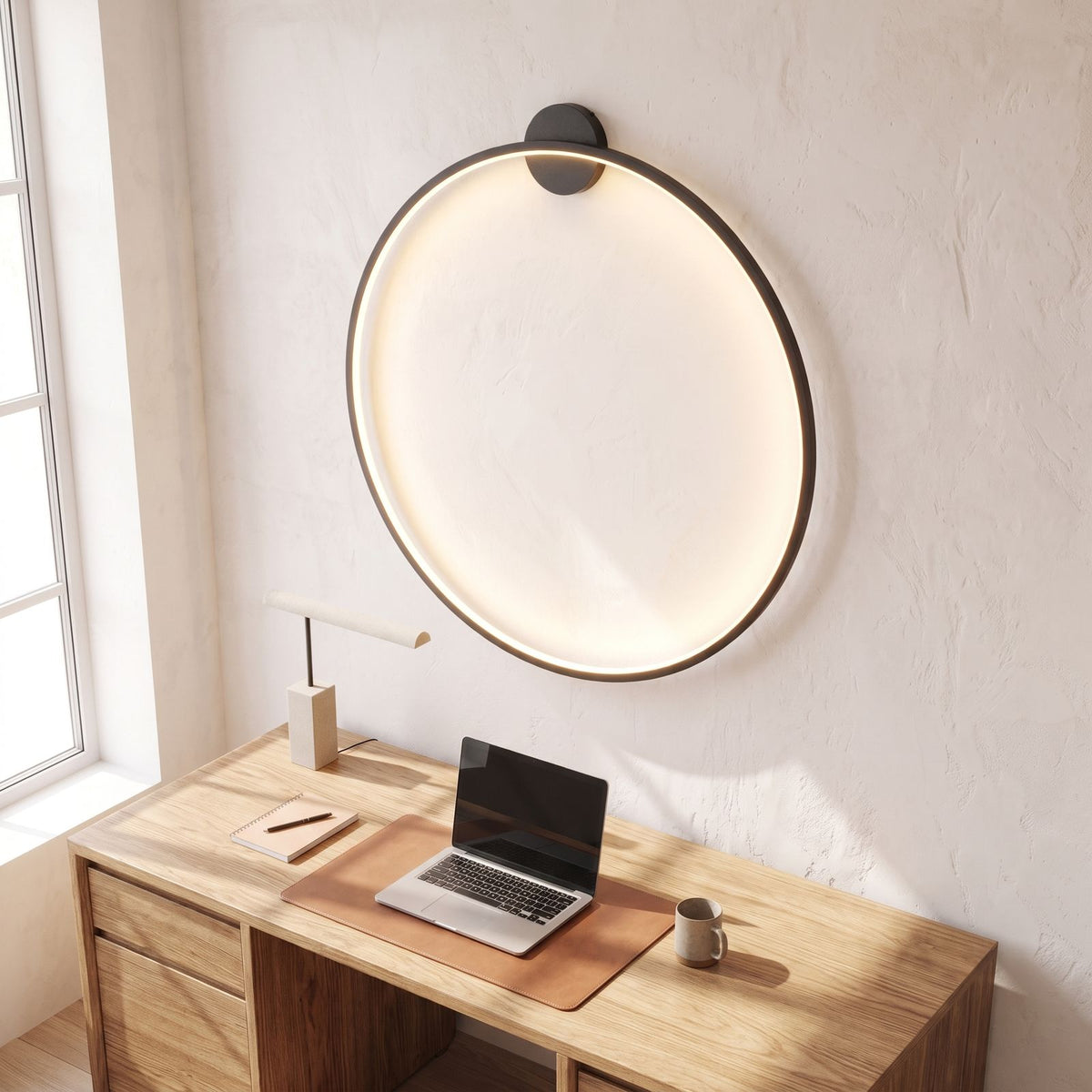 Slim black ring backlit LED wall light above a home office desk in daylight