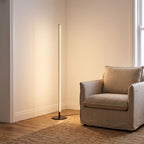Slim Linear LED Aluminium Floor Lamp beside an armchair in a living room corner