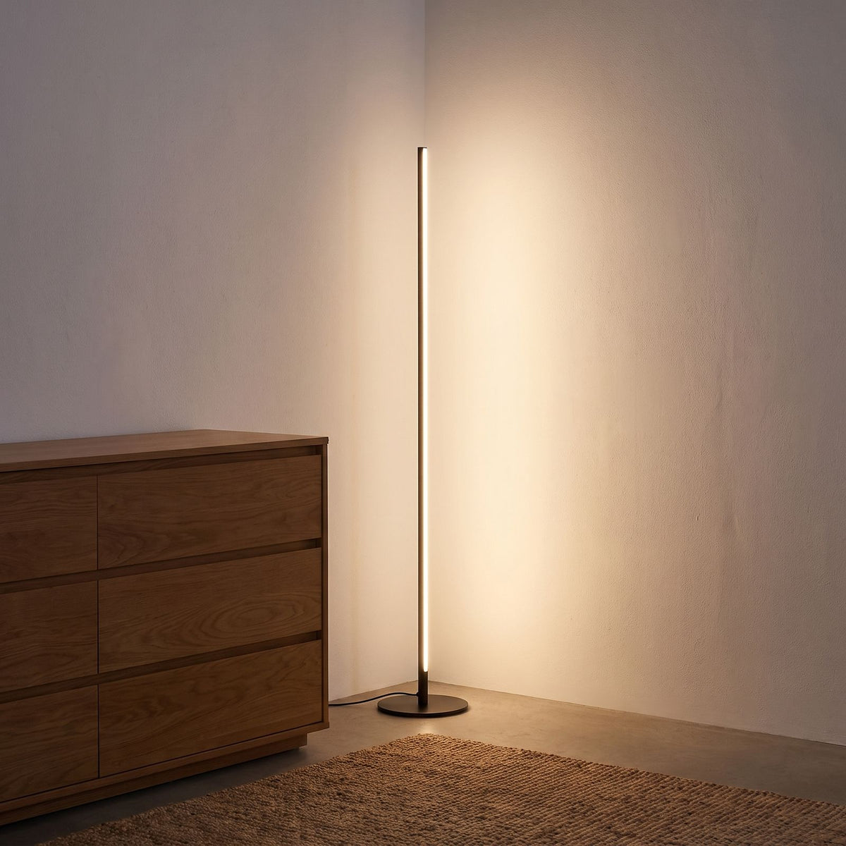 Slim linear LED floor lamp in a bedroom corner beside a dresser