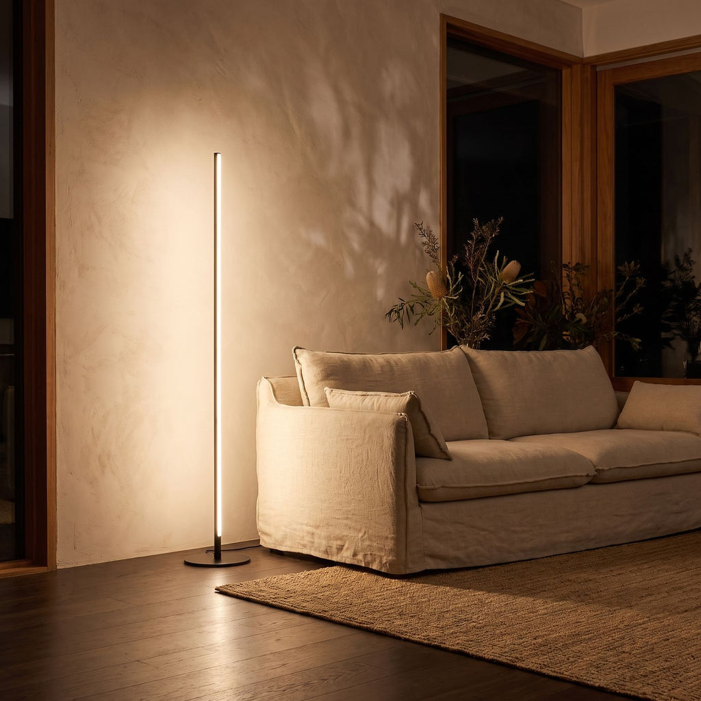 Slim linear LED floor lamp behind a sofa at night