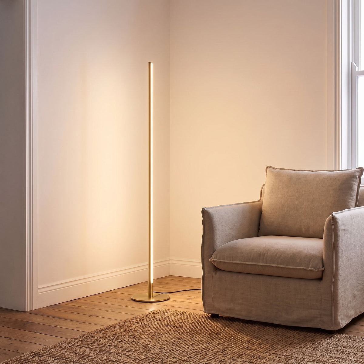 Slim Linear LED Aluminium Floor Lamp in gold beside an armchair in a living room corner