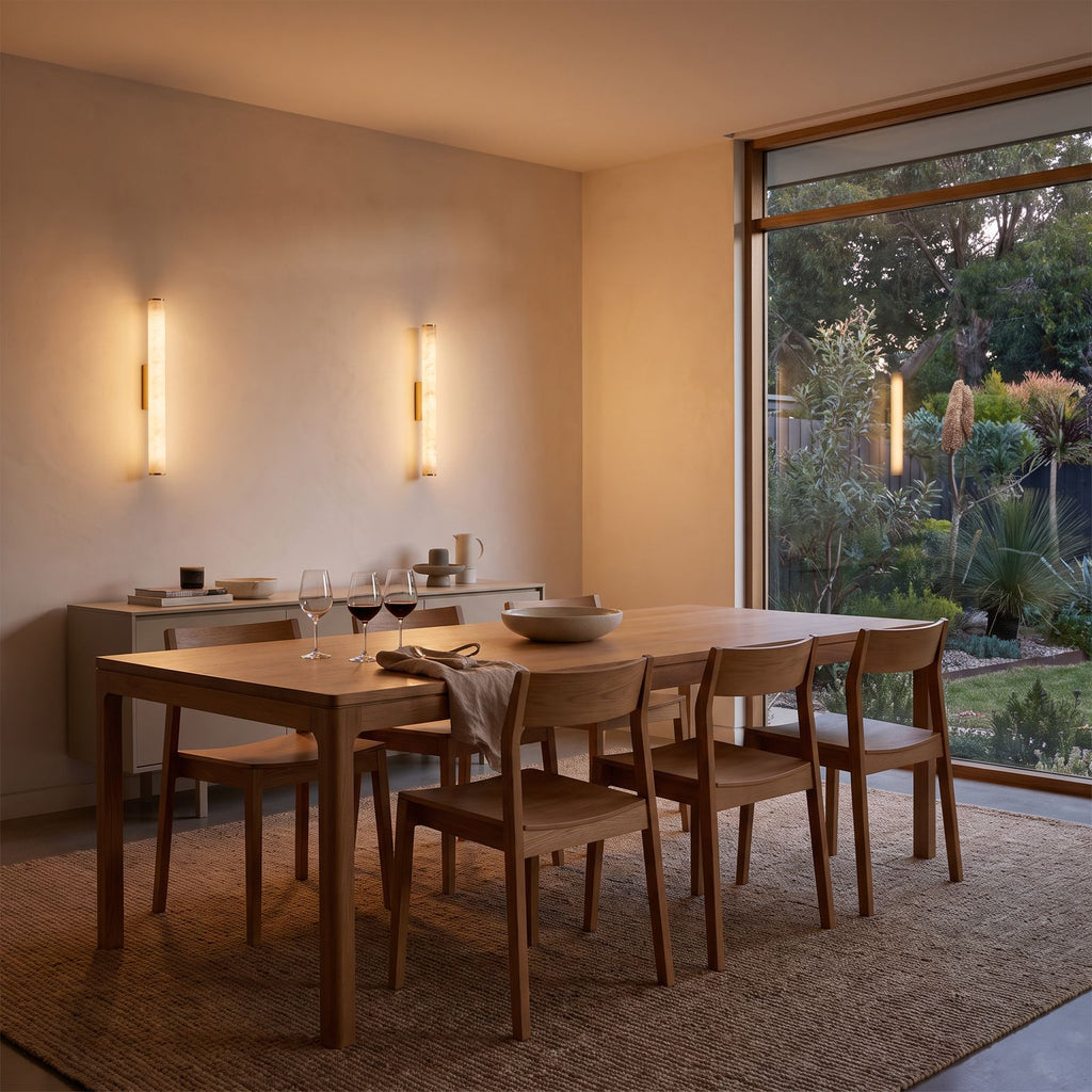 A pair of the marble tube wall lights above a sideboard in a dining room at dusk
