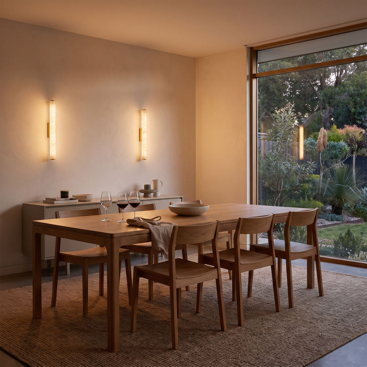 A pair of the marble tube wall lights above a sideboard in a dining room at dusk