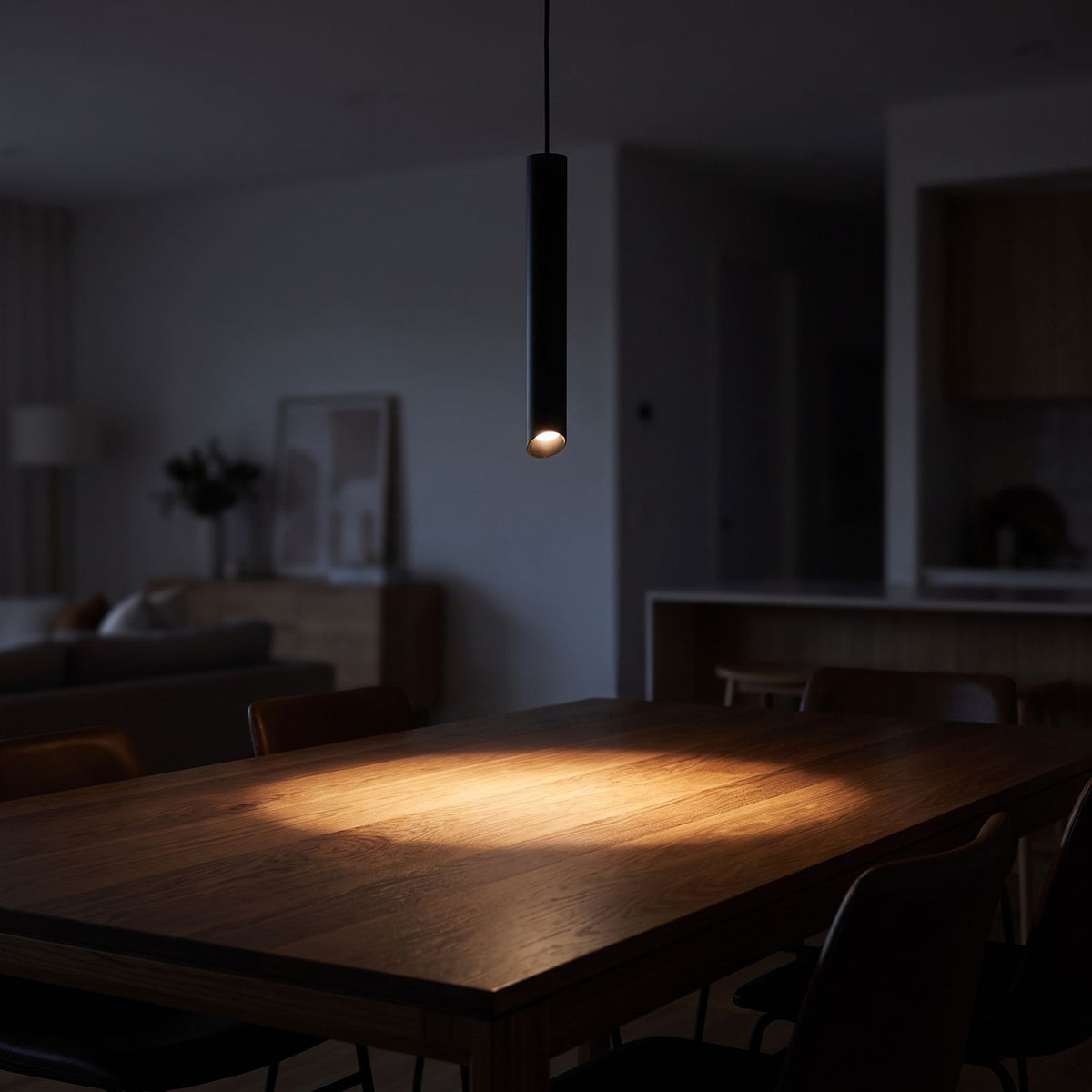 Slim metal cylinder pendant light over a dining table at night