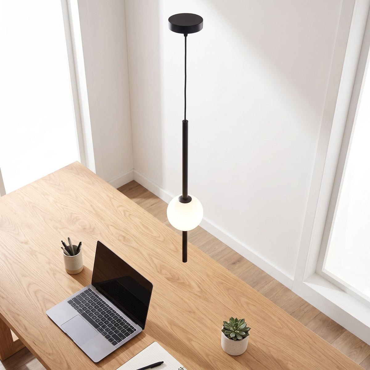 Slim rod frosted glass ball pendant light above a home office desk in daylight