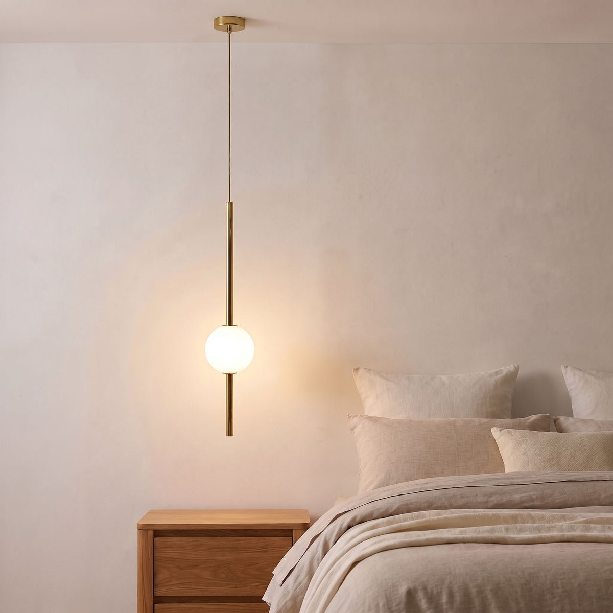 Slim Rod Frosted Glass Ball LED Pendant Light in brass beside a bed