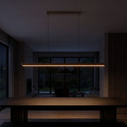 Slim wood bar linear LED pendant light over a dining table at night