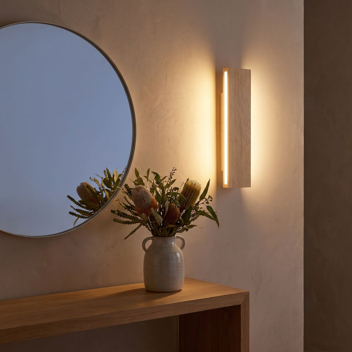 Slim wood plank wall sconce beside a round mirror in an entry hall