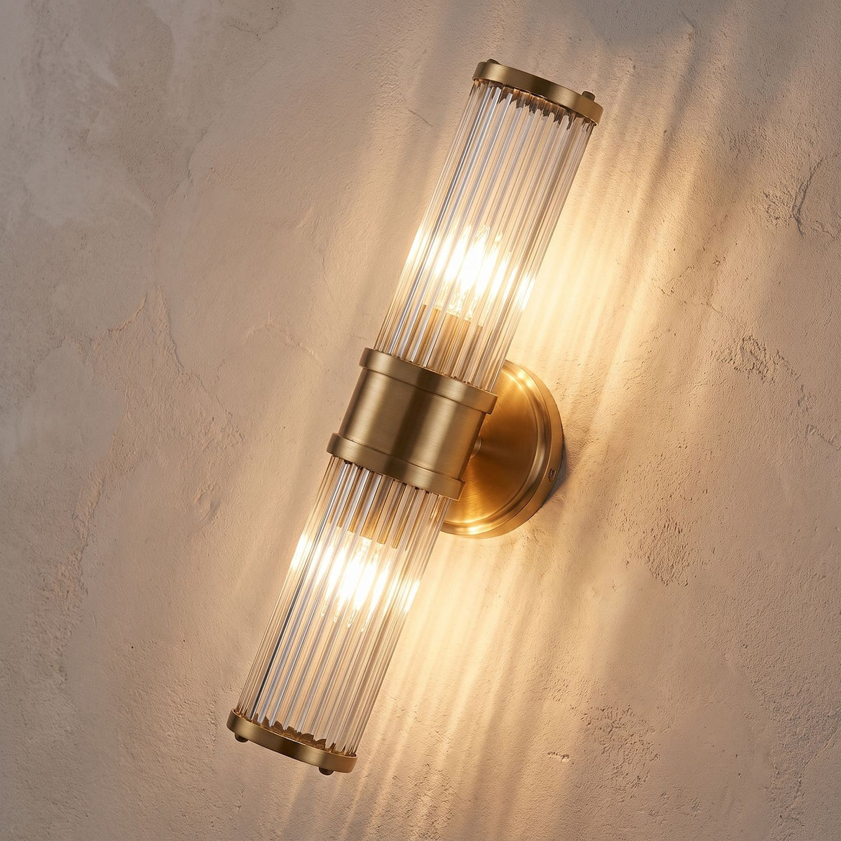 Ribbed Crystal Glass Tube Gold Wall Light with two tubes, close view at 45 degrees on a plaster wall