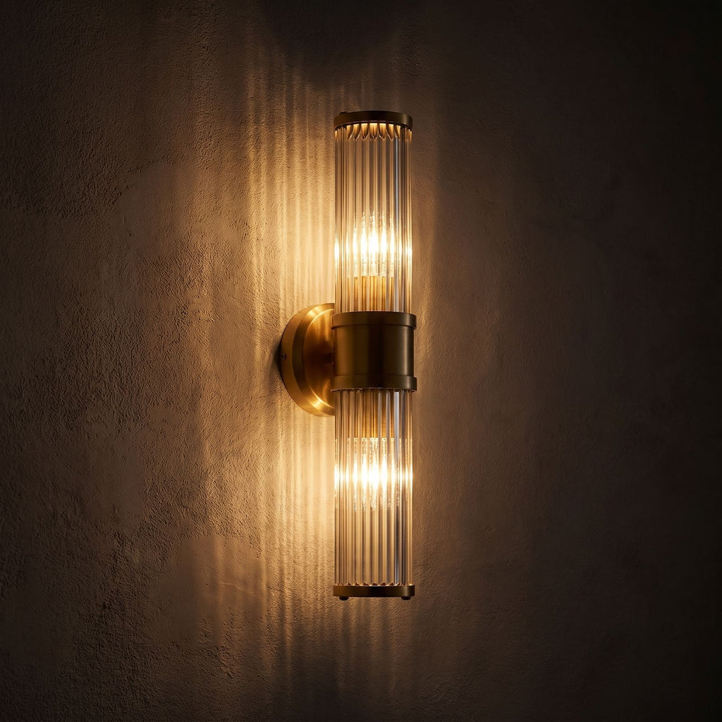 Ribbed Crystal Glass Tube Gold Wall Light with two tubes glowing on a plaster wall at night