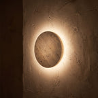 Solid Yellow Travertine Round LED Wall Light glowing on a plaster wall at night