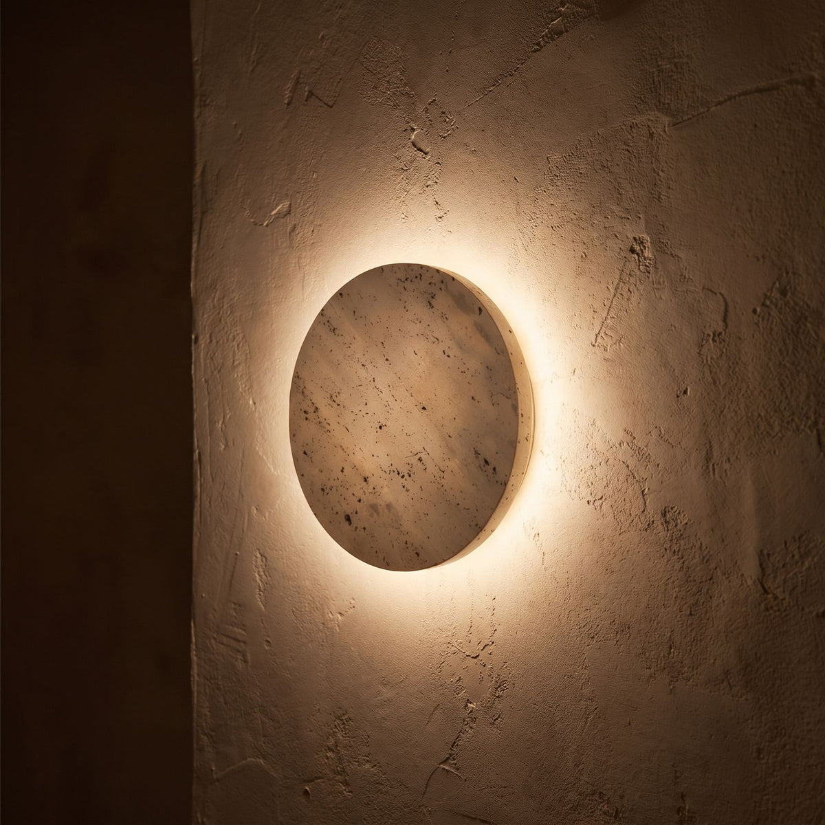 Solid Yellow Travertine Round LED Wall Light glowing on a plaster wall at night