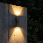 Square Cement Box Outdoor Wall Light glowing on a garden wall at night