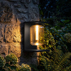 Square Frame Glass Outdoor Wall Lantern glowing on a garden wall at night