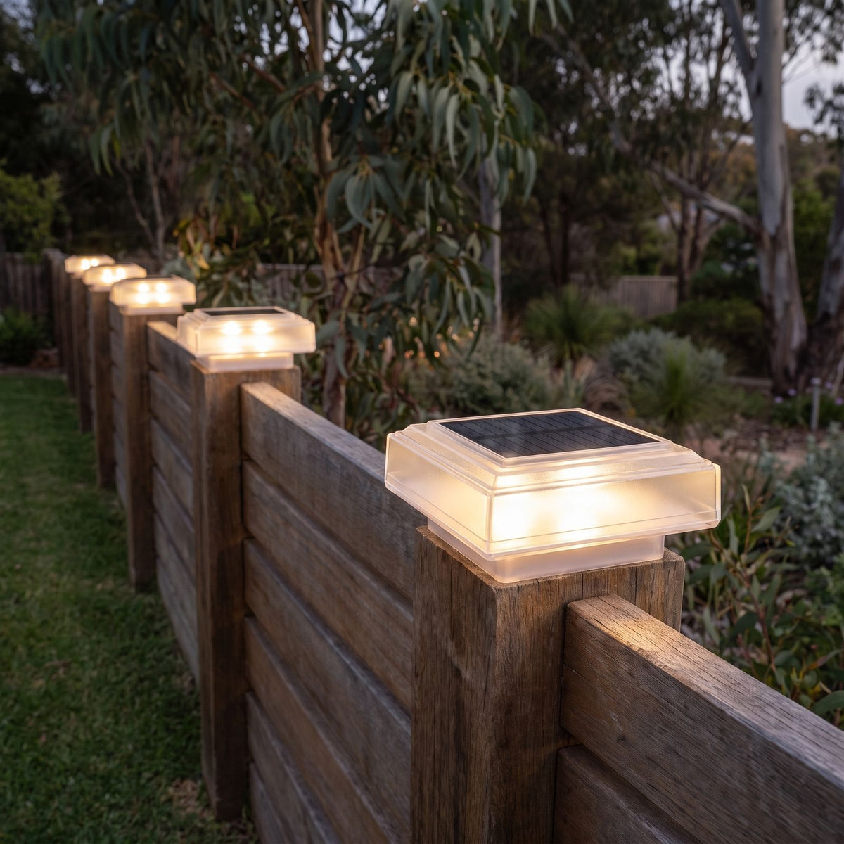 Square solar post cap light along a timber fence at night