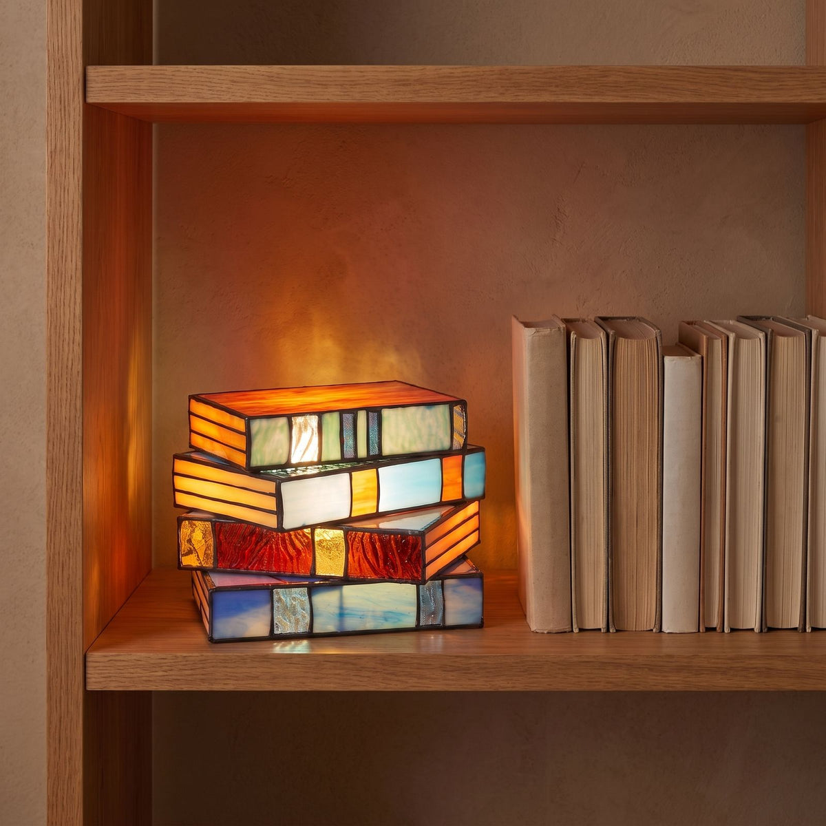 Stained glass stacked books table lamp on an oak shelf beside books