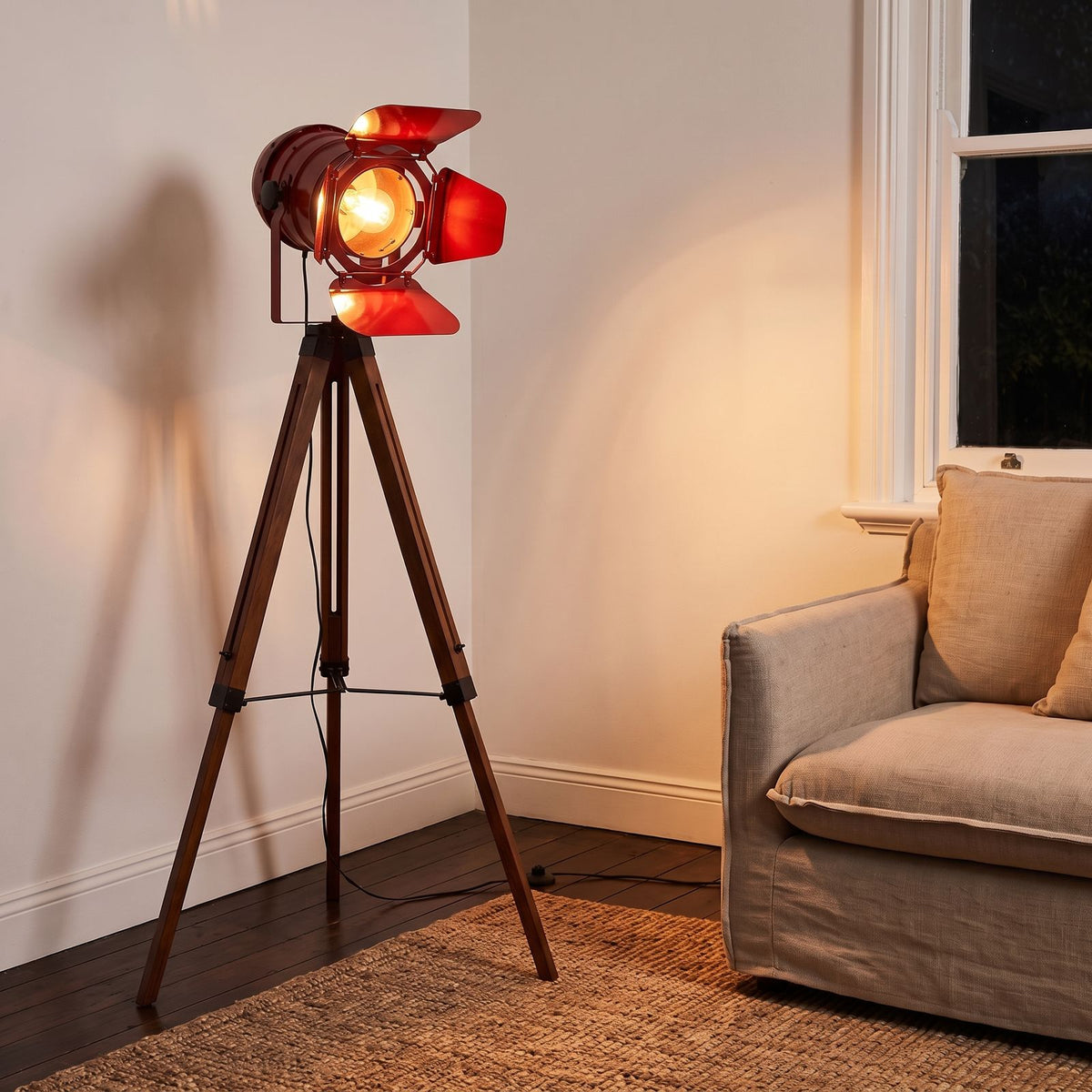 Studio Spotlight Wood Tripod Floor Lamp in red beside an armchair in a living room corner