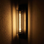Tall Black Iron Flute Edison Wall Light glowing on a plaster wall at night