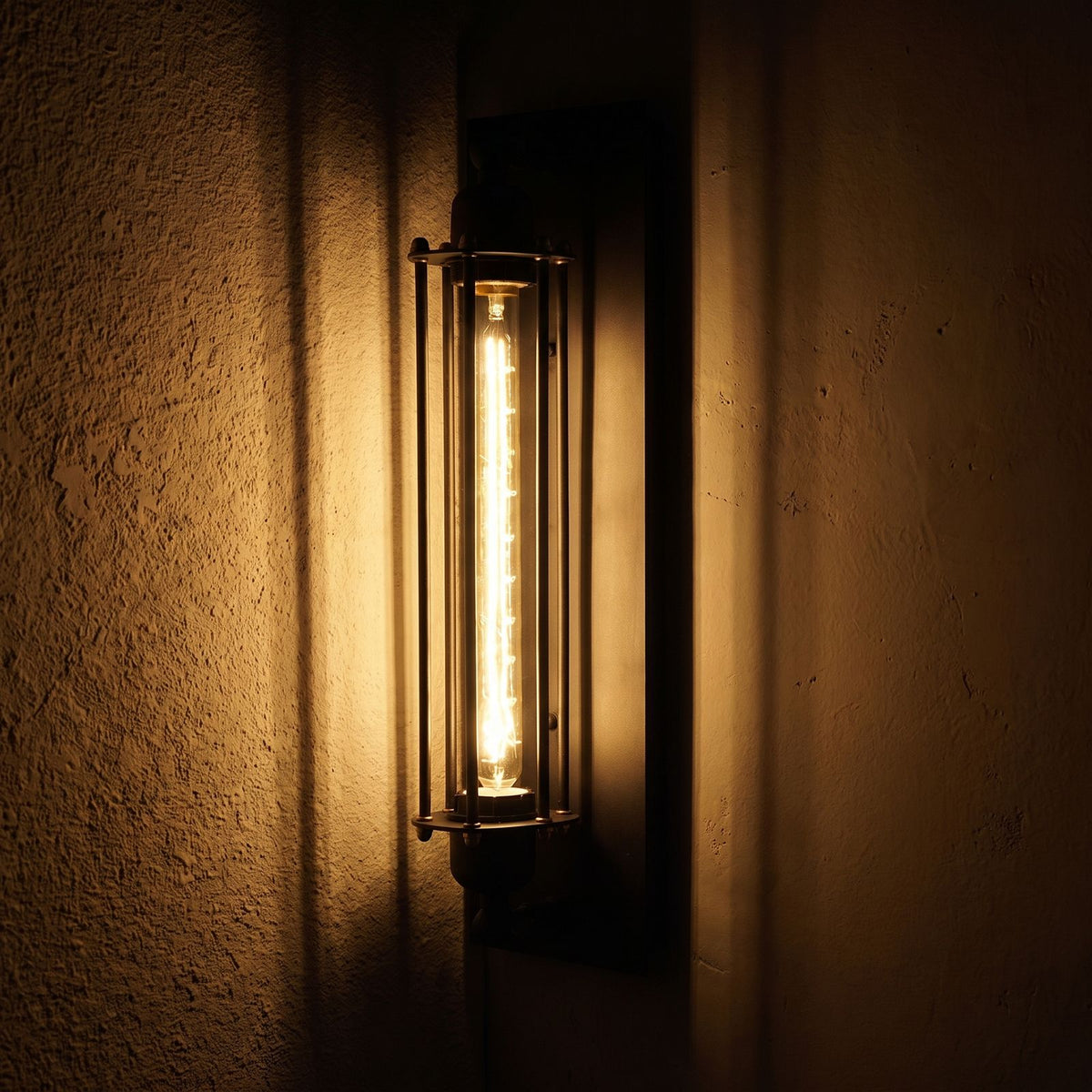 Tall Black Iron Flute Edison Wall Light glowing on a plaster wall at night