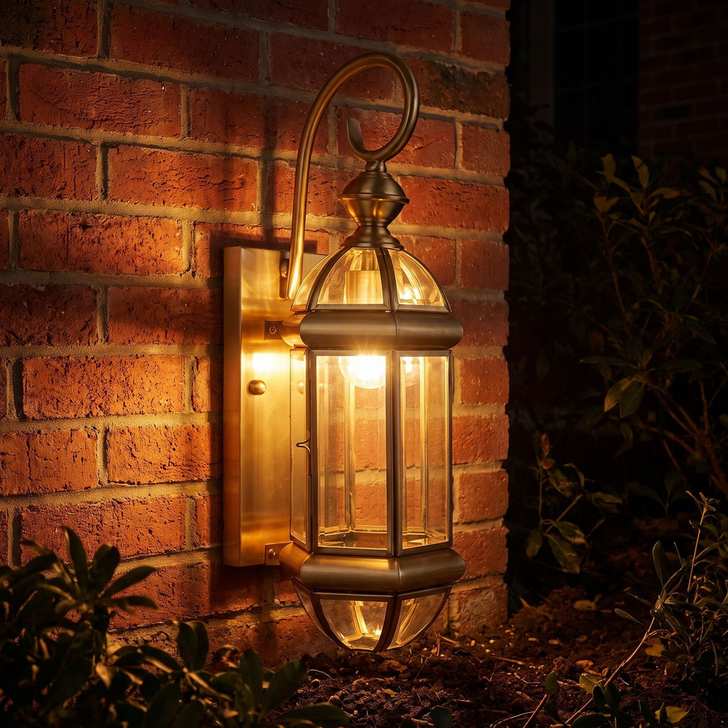 Tall Brass and Clear Glass Outdoor Wall Lantern glowing on a garden wall at night