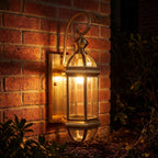 Tall Brass and Clear Glass Outdoor Wall Lantern glowing on a garden wall at night