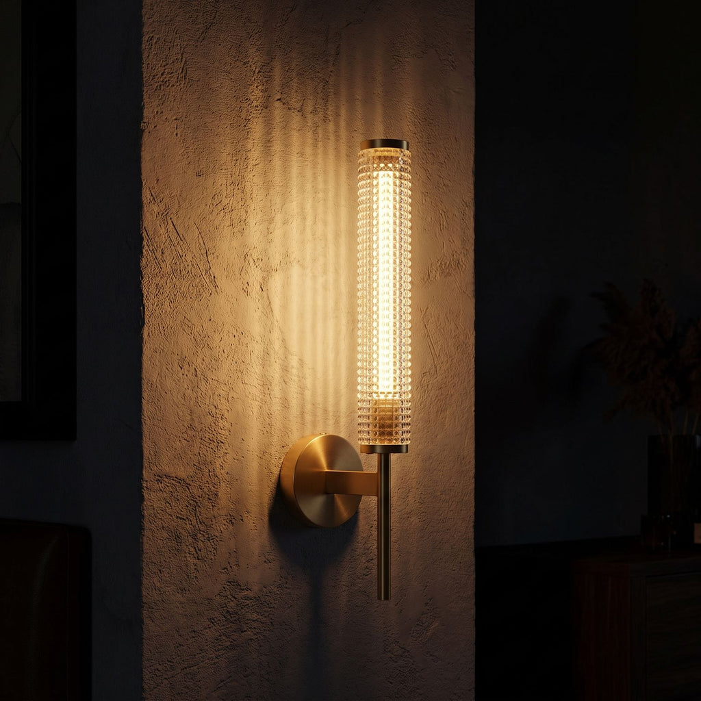 Tall Brass and Textured Glass Wall Sconce glowing on a plaster wall at night