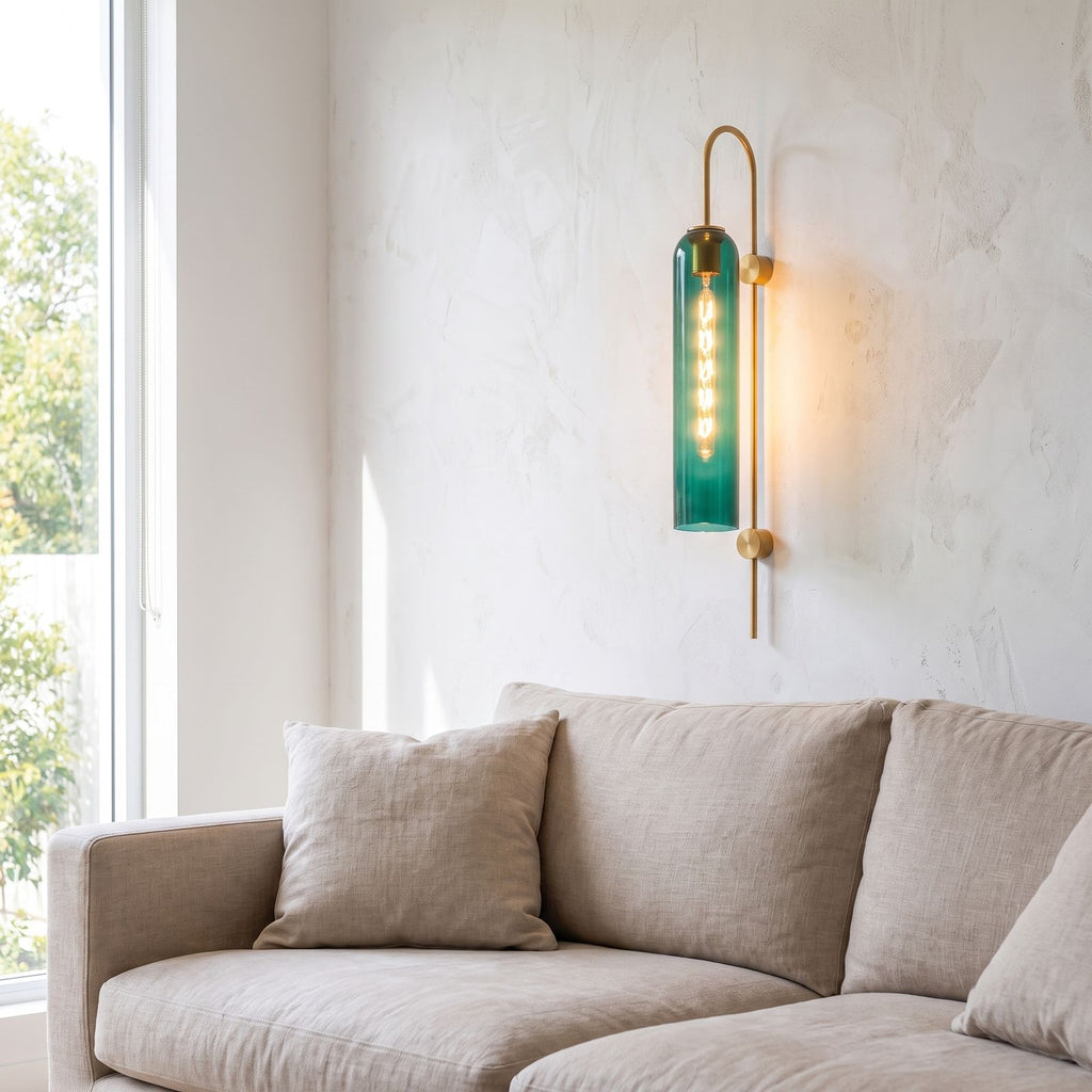 Tall hook arm glass cylinder wall light beside a living room sofa in daylight