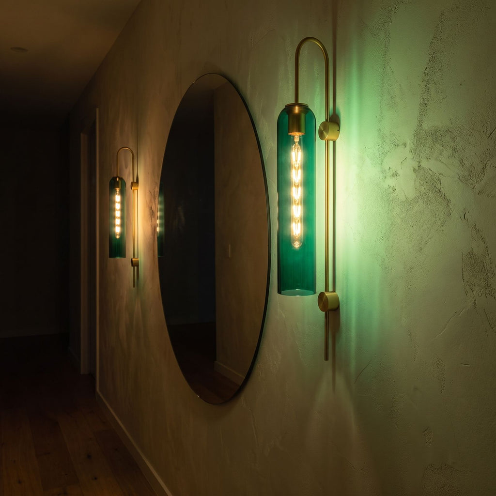 Tall hook arm glass cylinder wall light beside a round mirror in a hallway at night