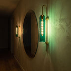 Tall hook arm glass cylinder wall light beside a round mirror in a hallway at night