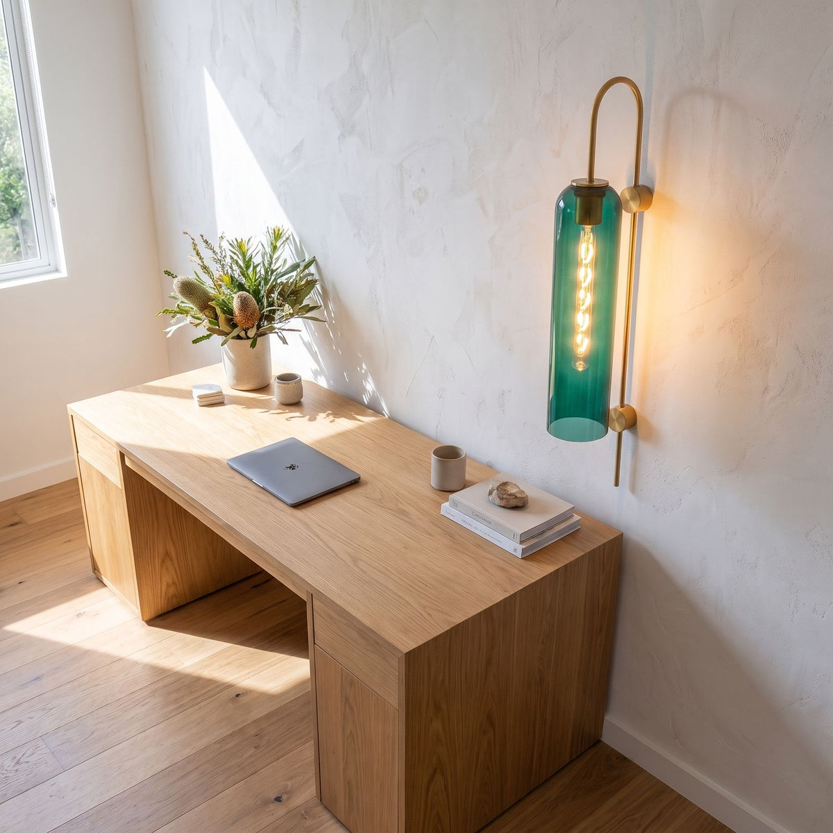 Tall hook arm glass cylinder wall light above a home office desk in daylight