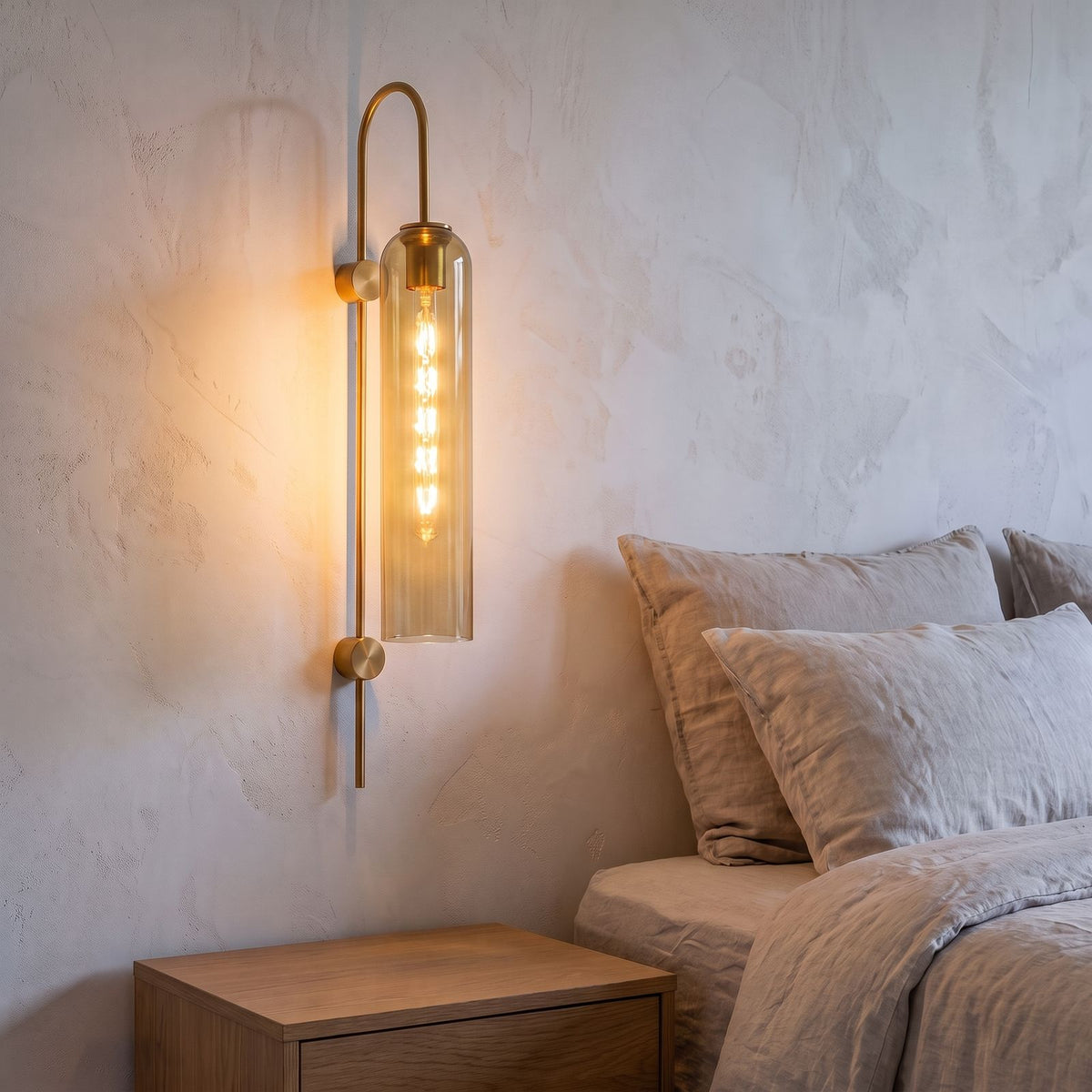 Tall Hook Arm Glass Cylinder Wall Light in amber glass beside a bed