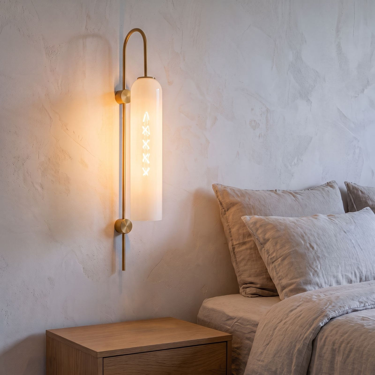 Tall Hook Arm Glass Cylinder Wall Light in white glass beside a bed