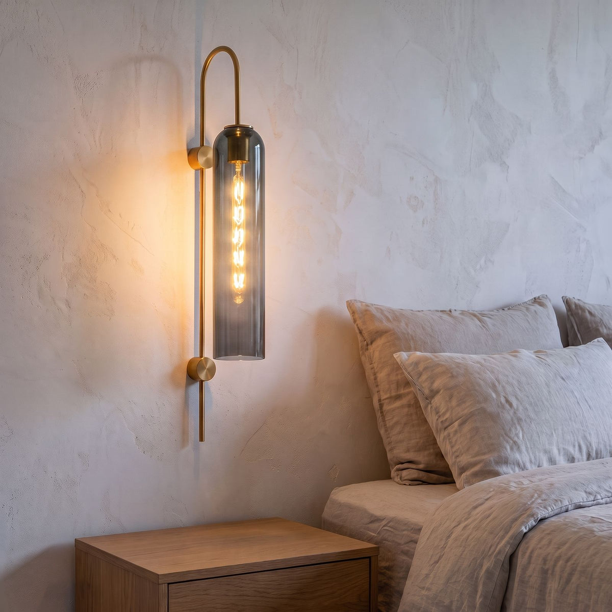 Tall Hook Arm Glass Cylinder Wall Light in smoke grey glass beside a bed