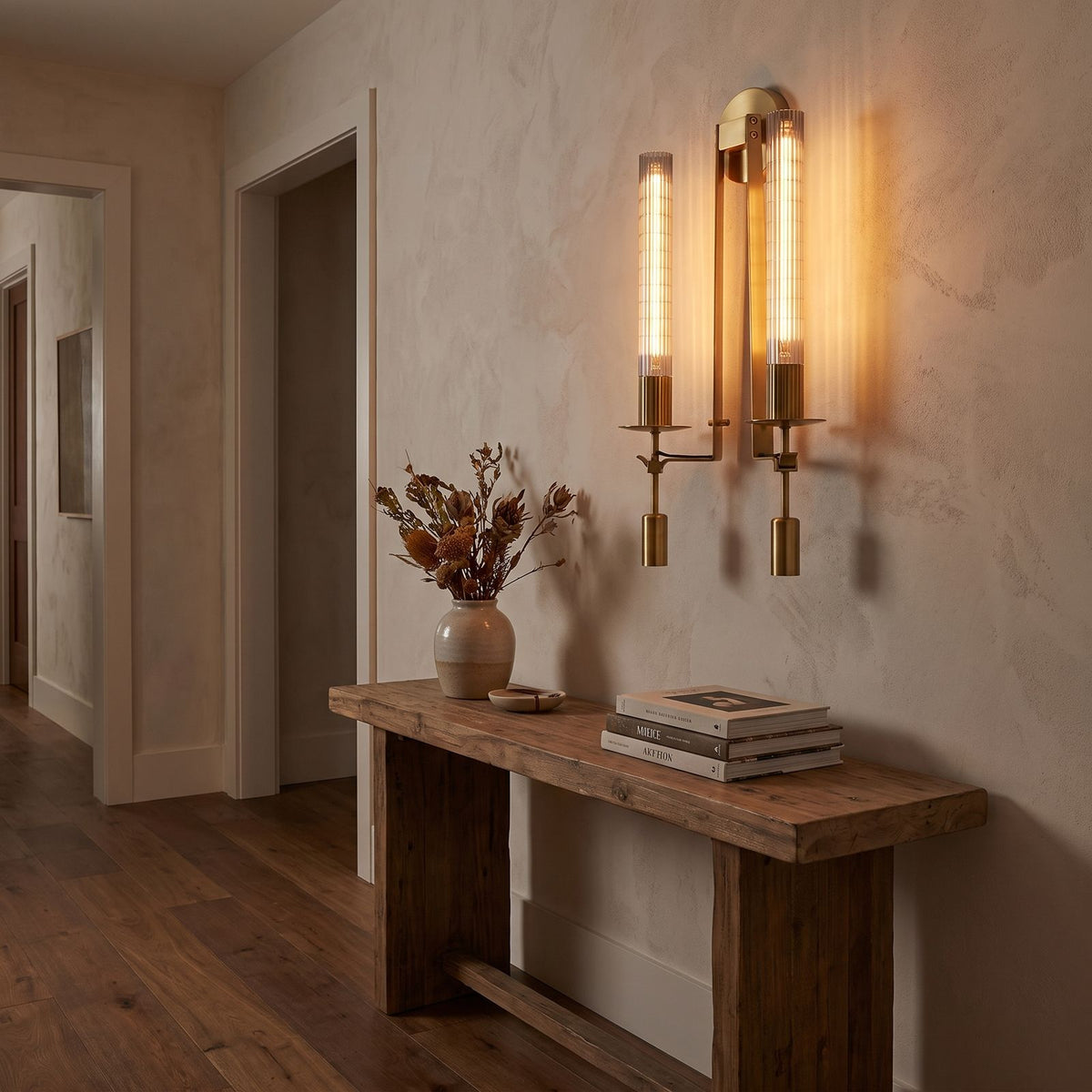 Tall Ribbed Glass and Brass Column Wall Light in a hallway above a timber console