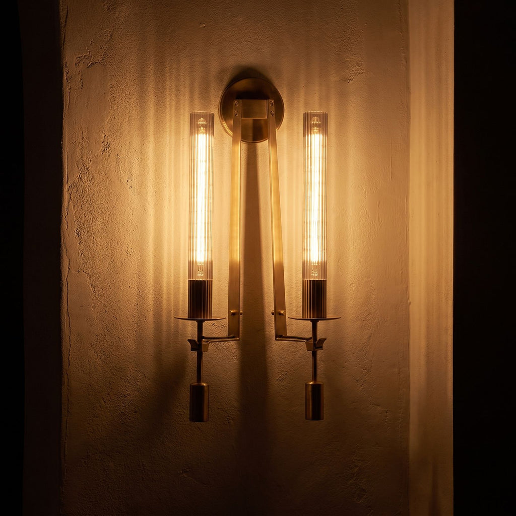 Tall Ribbed Glass and Brass Column Wall Light glowing on a plaster wall at night