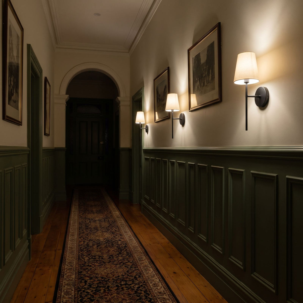 Three of the wireless wall sconces in black in a row along a hallway wall at night