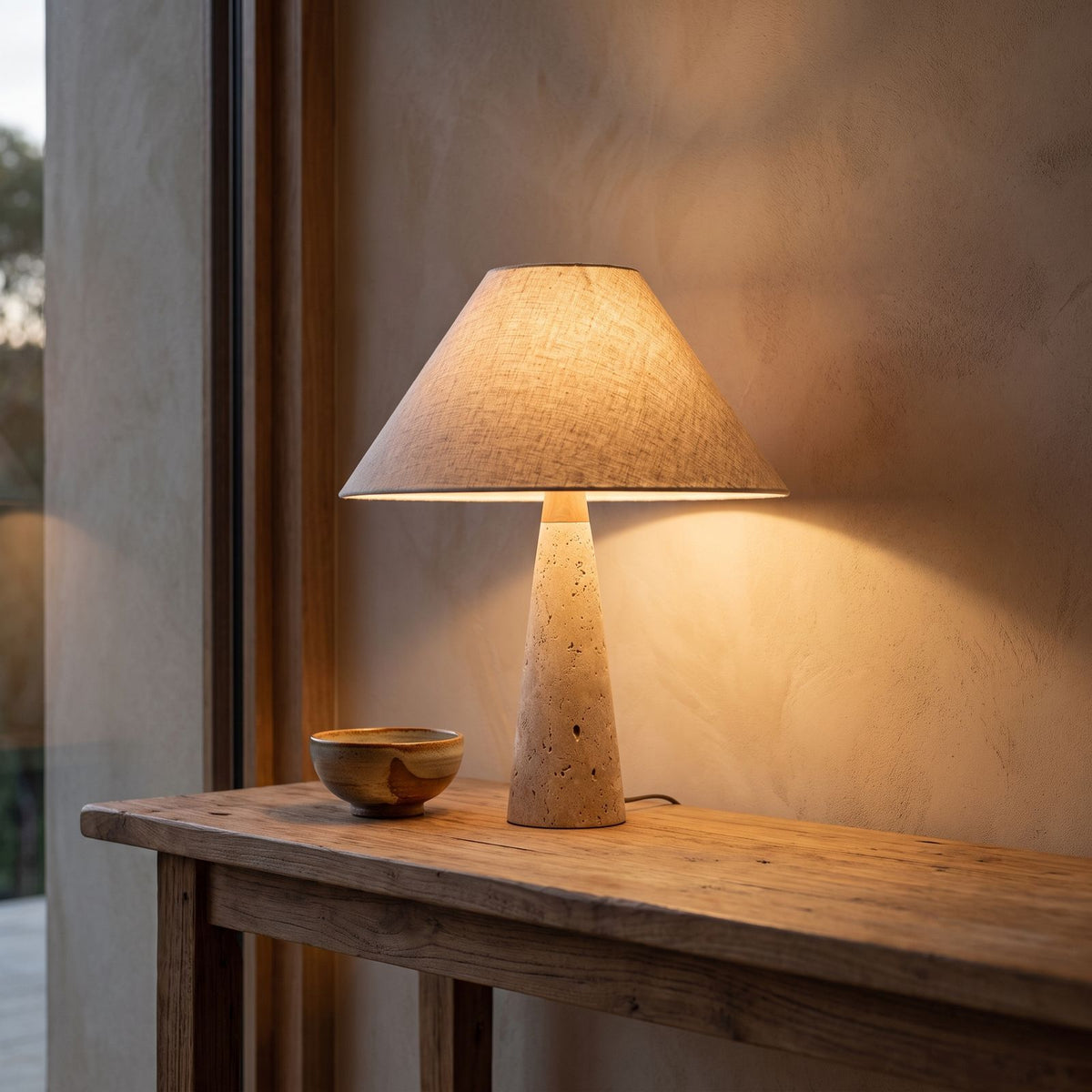 Tapered Travertine Stem Table Lamp glowing on a timber console at dusk