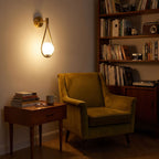 Teardrop Gold Frame Opal Glass Globe Wall Light above a velvet armchair in a reading corner at night
