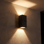 Textured Cement-Finish Box Wall Light glowing on a plaster wall at night