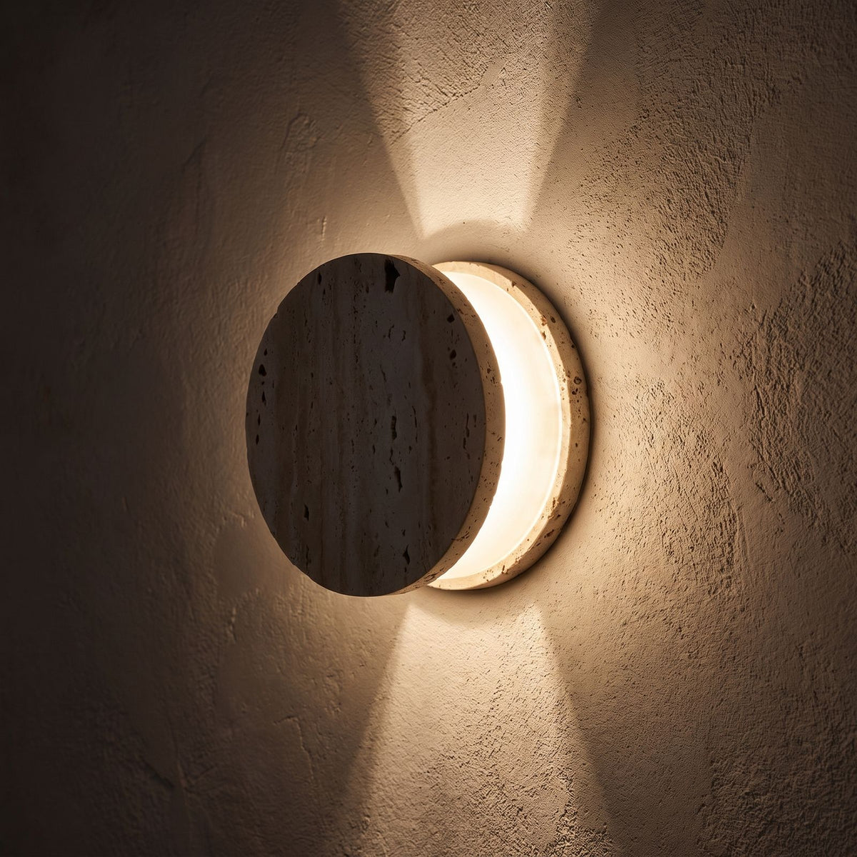 Travertine and Frosted Glass Up Down Wall Light glowing on a plaster wall at night