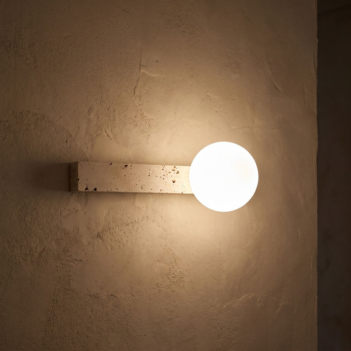 Travertine Bar and White Globe Wall Light glowing on a plaster wall at night