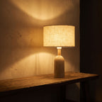 Travertine Base Fabric Shade Table Lamp glowing on a timber console at night