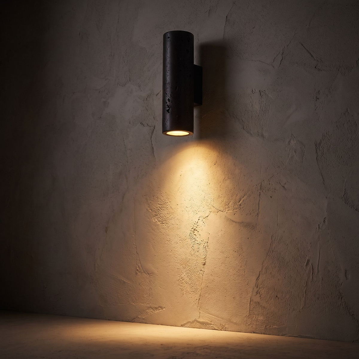 Travertine Cylinder Integrated LED Wall Light glowing on a plaster wall at night