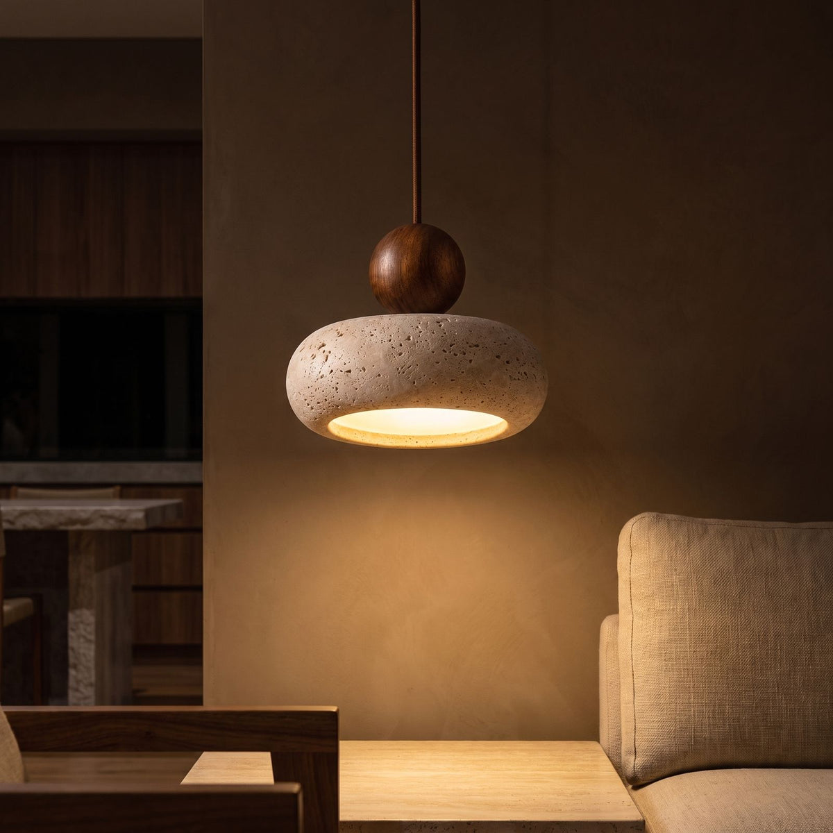 Travertine Donut and Wood Ball Pendant Light glowing against a plaster wall at night
