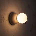 Travertine Half Dome Glass Orb Wall Light glowing on a plaster wall at night