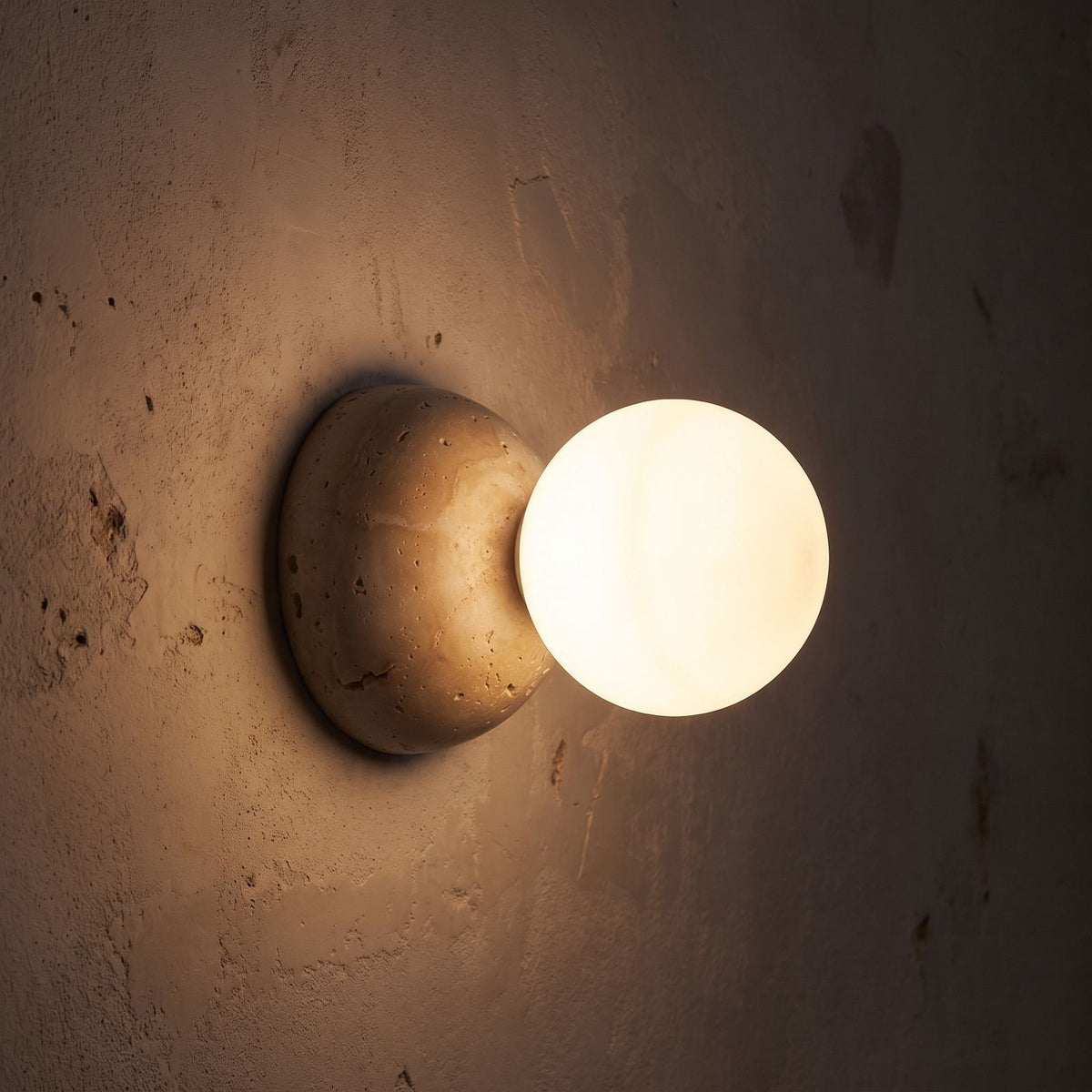 Travertine Half Dome Glass Orb Wall Light glowing on a plaster wall at night