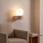Travertine ledge and frosted glass orb wall sconce above an armchair in a reading corner