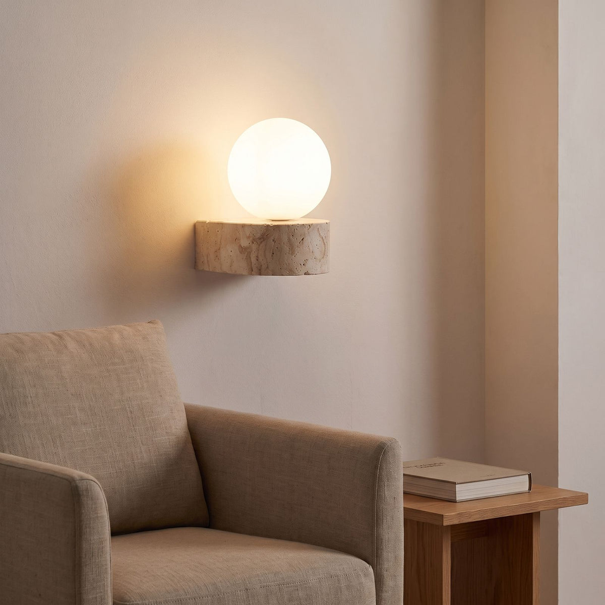 Travertine ledge and frosted glass orb wall sconce above an armchair in a reading corner